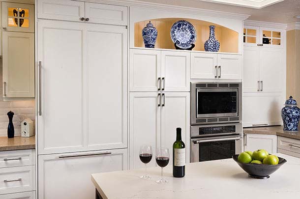 Kitchen island with wine bottle and two glasses of wine, ovens, white cabinets - large image